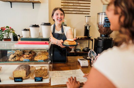 Happy barista serving delicious cinnamon roll to customer