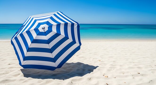 Blue and white striped beach umbrella standing on the sand with the ocean in the background on a sunny day. parasolka 