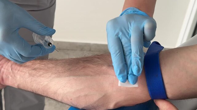 Nurse in blue latex gloves disinfecting visible vein and preparing needle for blood collection close up medical procedures, laboratory testing, hygiene, and patient care during venous blood sampling.