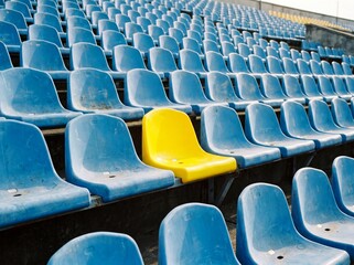 Fototapeta premium Bright yellow stadium seat stands out among blue chairs in isolation