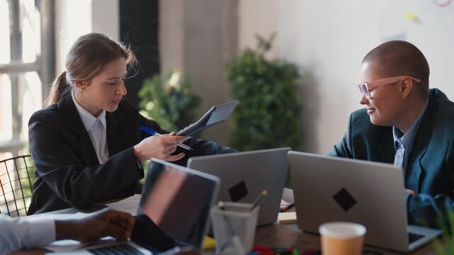 Positive atmosphere in office, colleagues discussing in co-working area, woman. Smiling ladies talking about work sitting at table in conference room, marketing and financial professionals, good mood
