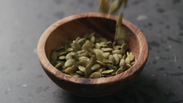Slow motion dried pumpkin seeds falling into olive bowl on terrazzo countertop