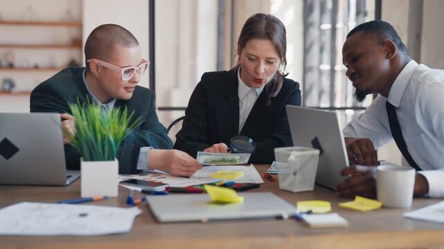Team of marketing professionals working together in office, medium portrait. Young adult people sitting at table and examining reports and data of financial researches, business meeting in conference