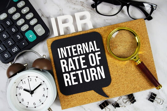 IRR - Internal Rate of Return acronym with calculator, alarm clock and magnifying glass, business concept background