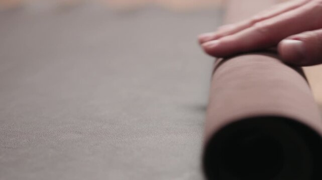 Slow motion man unroll brown leather piece on walnut table closeup