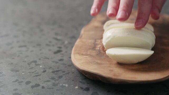Slow motion man slicing fresh mozzarella cheese on olive wood board