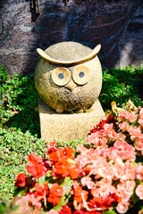 schöne Eule auf einem Sockel hinter bunten Blumen auf einem Friedhof in Köln © Blende8