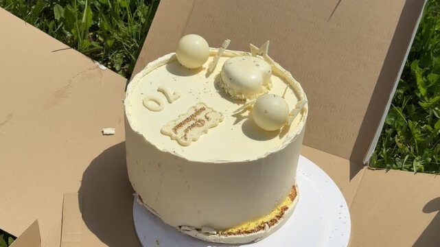 fixing a damaged birthday cake box after a white 70th birthday cake fell on grass outdoors