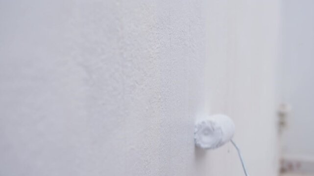 Close-up of paint roller applying fresh white paint on terrace wall during home renovation and exterior improvement work.Home improvement and renovation project show painter doing interior decoration