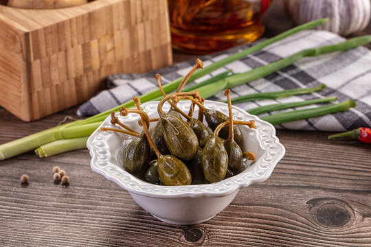 Pickled caper berries in a bowl with fresh ingredients on a rustic wooden table.