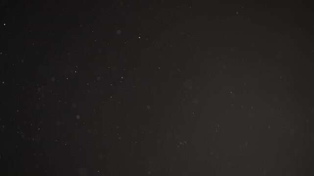 Slow motion real dust particles floating mid air over dark background