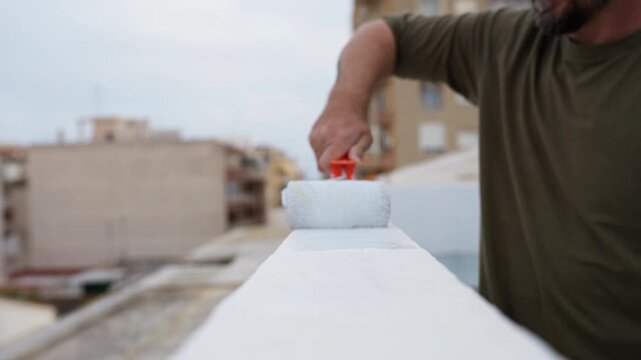 Close-up Builder with a paint roller carefully applying fresh coat of white waterproofing paint on rooftop terrace, protecting surface during home renovation