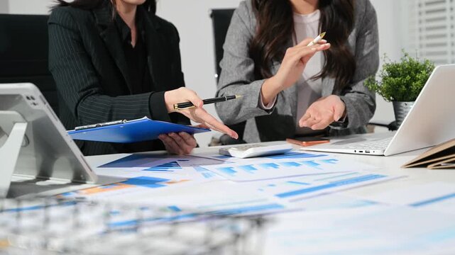 Two professional businesswomen collaborate, analyzing financial charts and counting reports