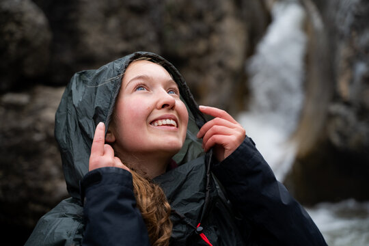 A young smiling woman is putting on a raincoat before it starts to rain outdoors, using protective clothing to protect herself from bad weather.

