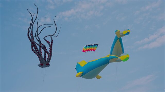 Colorful kite festival with giant inflatable kites flying in blue sky, outdoor event with large animal shaped squids and whales floating in wind under clouds 4k