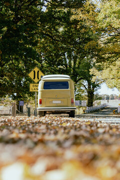 Vintage camper van parked on a quiet autumn road surrounded by colorful trees and fallen leaves capturing retro travel, road trip adventure outdoor lifestyle, freedom, and seasonal nature scenery.
