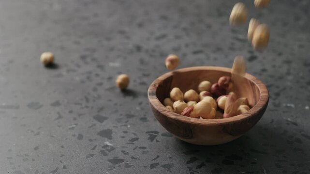 Slow motion roasted hazelnuts falling into olive bowl on terrazzo countertop