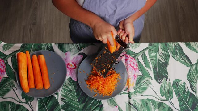 Detailed close up of woman grating fresh carrot with hand grater during cooking process using natural vegetables for healthy homemade dishes. High quality 4k footage