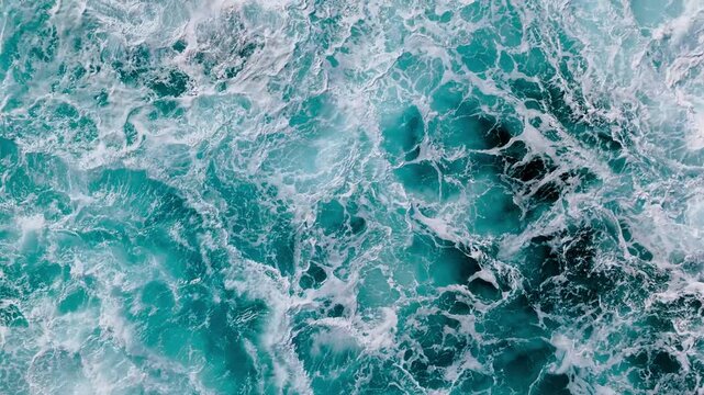 Top view of active ocean water with foam and swirling currents and breaking waves