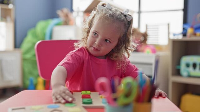 Girl placing colorful wooden puzzle pieces with hand on a play table in a building; curiosity learning.