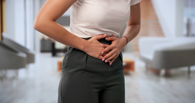 Young Woman Sits On Sofa Feeling Stomachache
