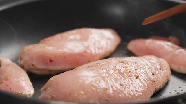 Slow motion man hand turn chicken fillet on non stick pan closeup