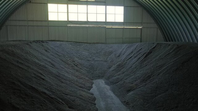 Cinematic movement inside agricultural warehouse with massive sunflower seed storage piles in industrial hangar