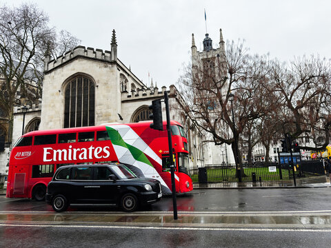 Red Emirates double decker bus and black cab pass a historic church in London, UK on a rainy day