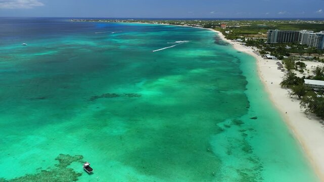 Drone pans left while tracking a jet ski along Seven Mile Beach near Kimpton Seafire Resort in Grand Cayman