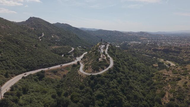 Scenic mountain landscape of Simi Valley California with winding road and cars driving along green hills near Santa Susana Pass under blue sky with expansive valley. Aerial establishing wide shot.