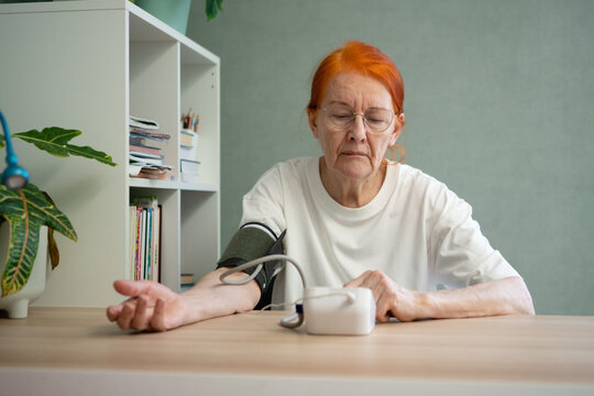 A senior lady is seated at a table, patiently waiting for the outcome of her blood pressure measurement on the tonometer. This daily checkup is crucial for managing health