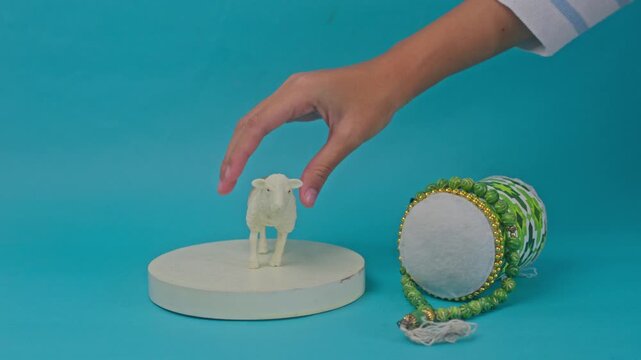 Hand places sheep figurine on pedestal next to bedug drum and prayer beads for Eid al-Adha