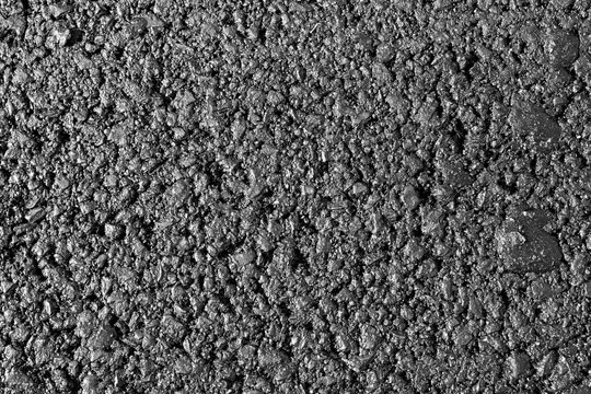 Close-up image of an asphalt surface featuring small stones and gravel, highlighting the rough texture and durability of this construction material