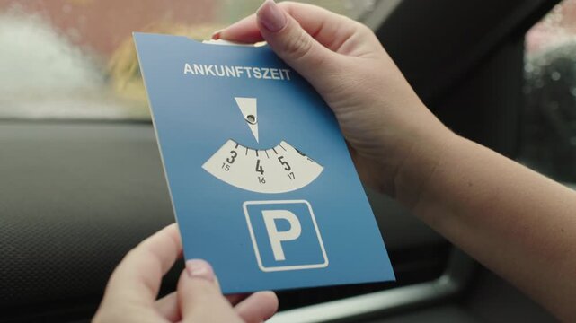 Driver holding German parking disc with word Ankunftszeit meaning arrival time inside parked car