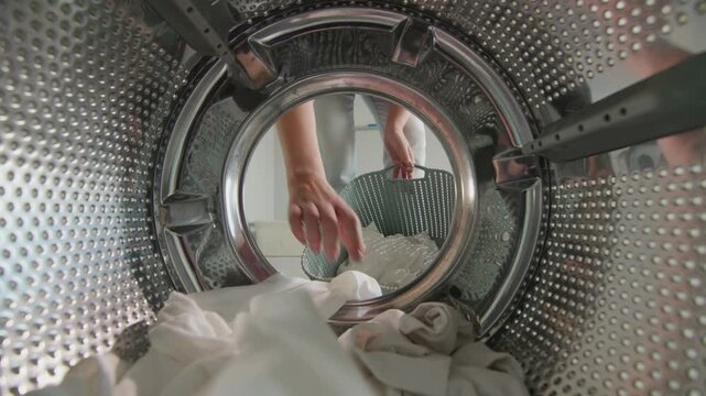 Person placing laundry items inside metal washing machine drum from internal view.