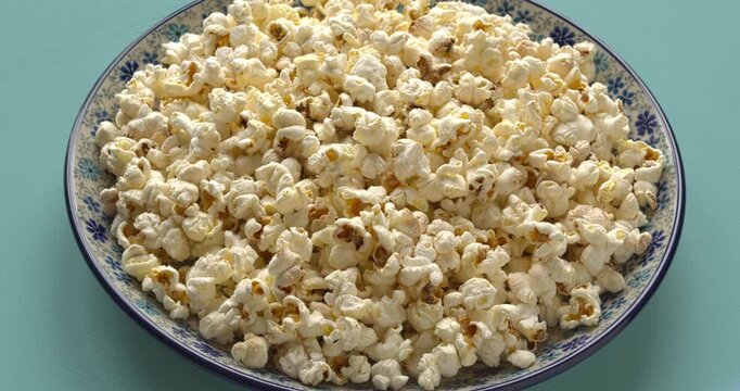 A plate with freshly made popcorn, a blue background, and a table spin.