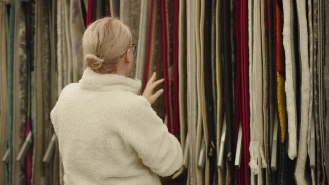 Woman choosing carpet and textile samples in home decor store with colorful fabric rolls and interior design materials