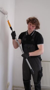 Vertical screen exhausted house painter struggles to stay awake during apartment renovation tired worker pauses with paint roller after long hours indoors