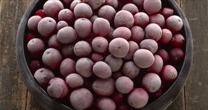 A bowl with frozen cranberries. Rustic wooden background. Table spin.