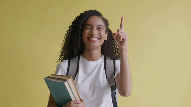 Happy student holding books and pointing up on yellow background