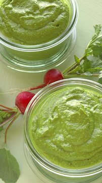 Two glass jas with radish greens pesto and fresh, whole radishes next to them - vertical video.