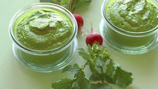 Two glass jas with radish greens pesto and fresh, whole radishes next to them - light green background.