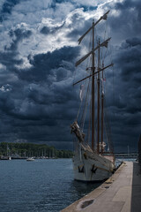 Fototapeta premium A sailing ship in the harbor of Travemünde, set against an approaching, dramatic storm front