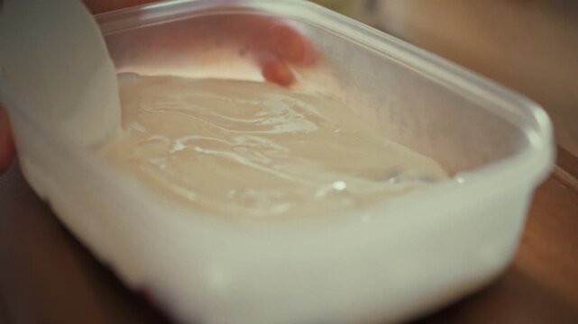 In cozy home kitchen, housewife leisurely whips up batch of homemade ice cream. She carefully adds dollop of whipped cream to special ice cream mold, savoring sweet process of crafting frozen treat