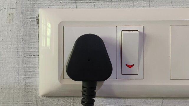 Closeup of hand pushing electric appliance three pin plug into indian power outlet or socket hole on wall and switch on the equipment. Daily household electricity consumption and use concept.