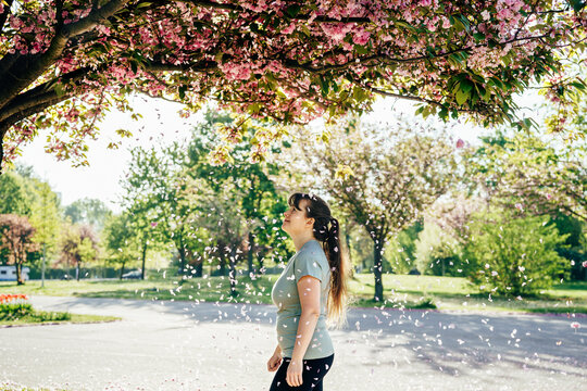 Young woman enjoying falling cherry blossom petals in sunny spring park