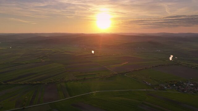 Spectacular aerial view of parceled agricultural fields with working tractors and a winding river in a picturesque rural landscape at sunset, forward tracking drone shot, graded