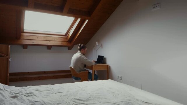 Man working remotely in attic apartment cozy home office lifestyle
Wide shot of man working remotely from attic apartment with laptop in cozy home interior. Modern remote work lifestyle and digital no