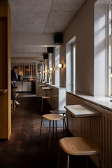 Fotobehang Horeca Minimalist Scandinavian cafe interior in Denmark with wooden stools, window seating, warm lights and cozy hygge atmosphere  © Bastian
