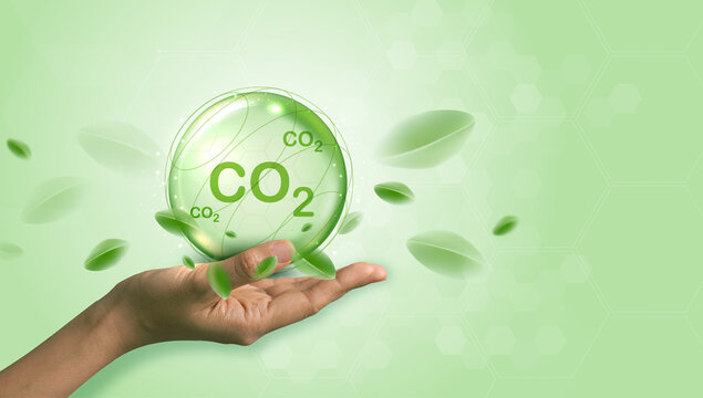 Hand holding glowing green CO2 sphere with flying leaves on light green background. Carbon dioxide reduction, net zero emissions, eco-friendly sustainable green technology and environment concept.